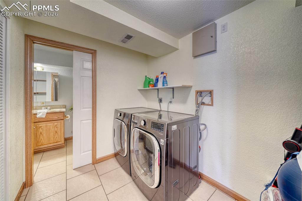 Laundry room featuring separate washer and dryer, a textured ceiling, a textured wall, and light tile patterned floors