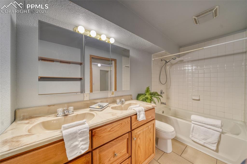 Full bath with double vanity, shower / bath combination, and light tile patterned floors