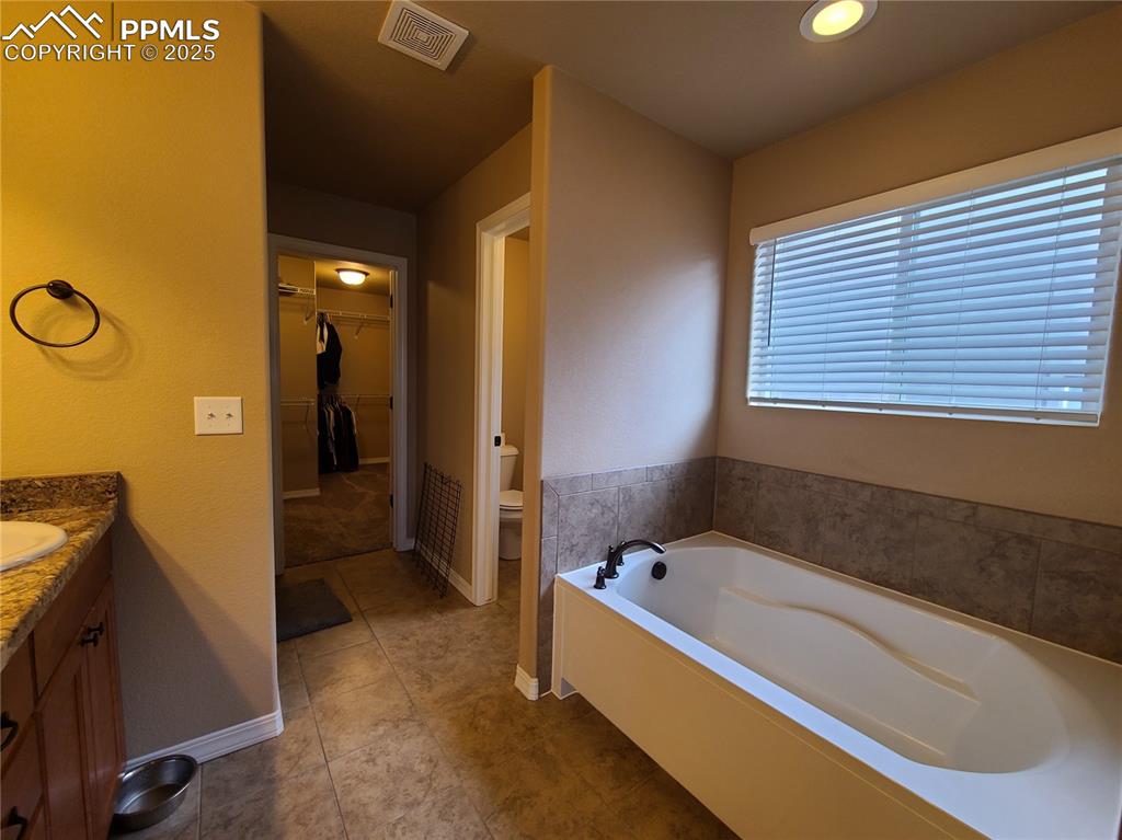 Full bathroom with vanity, a bath, a spacious closet, and dark tile patterned floors