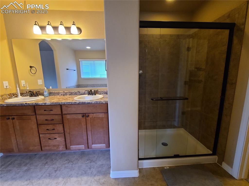 Full bathroom with a stall shower, light tile patterned floors, and double vanity