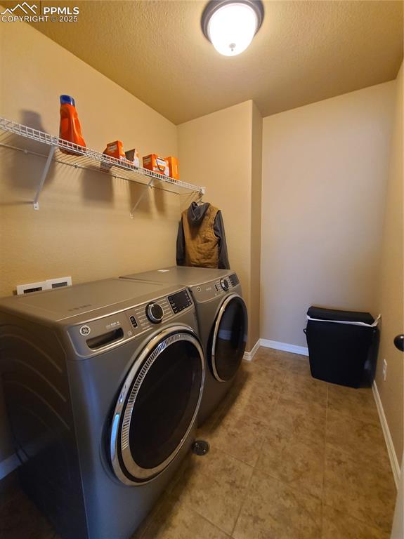 Laundry area with separate washer and dryer, light tile patterned floors, and a textured ceiling