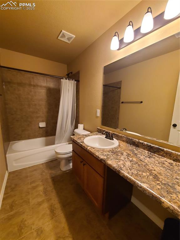 Bathroom with shower / bath combo with shower curtain, vanity, and dark tile patterned flooring