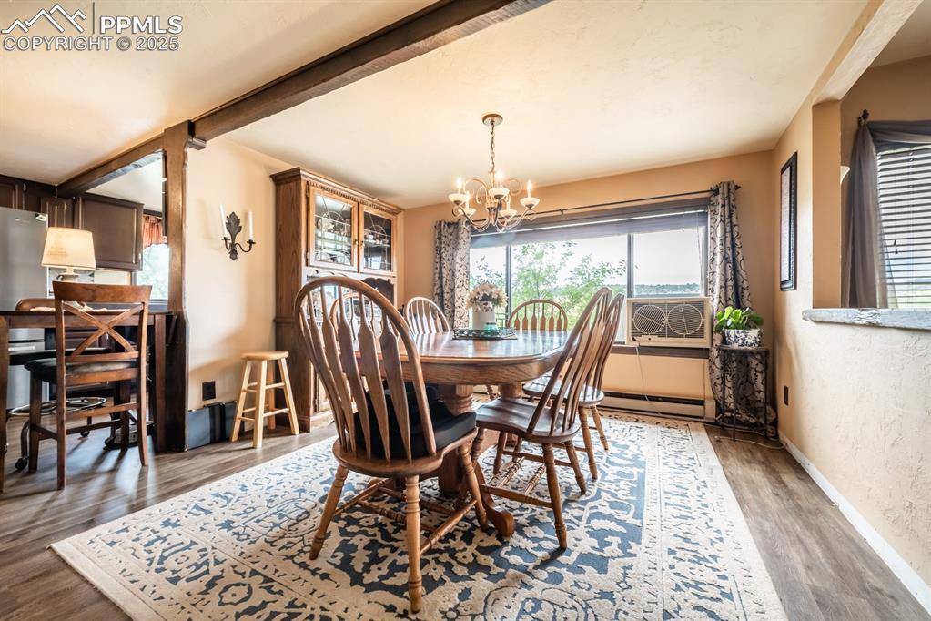 Dining space with dark hardwood / wood-style flooring, baseboard heating, cooling unit, beam ceiling, and an inviting chandelier