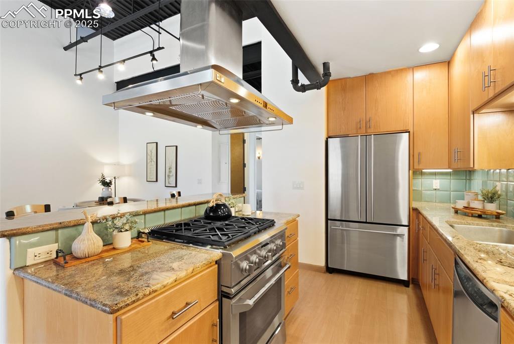 Kitchen with stone counters, stainless steel appliances, an island with a gas stove top, and range