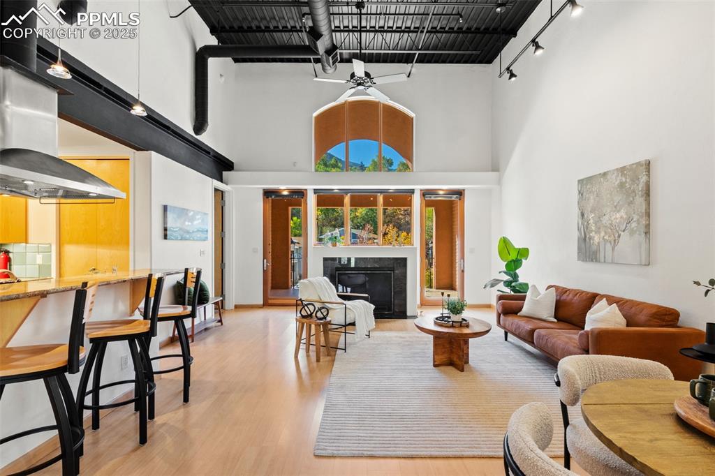 The living area featuring light wood-style flooring, a tiled fireplace, and an industrial accent ceiling