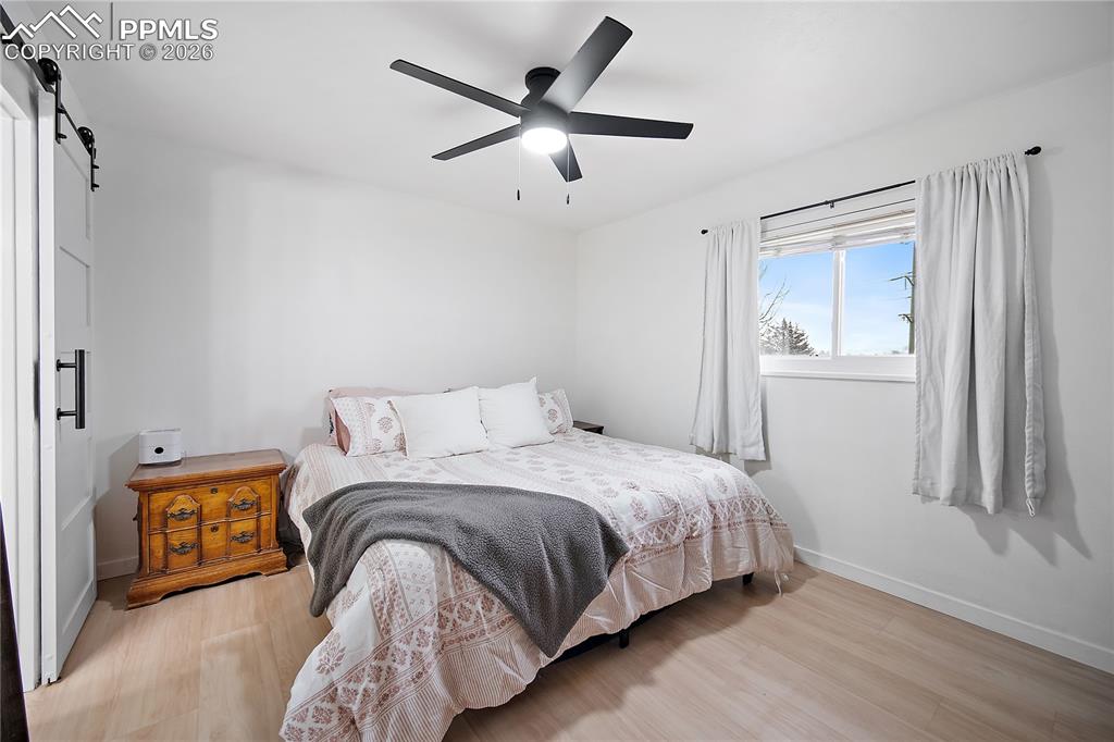 Main level primary bedroom with laminate flooring, large window and ceiling fan. 