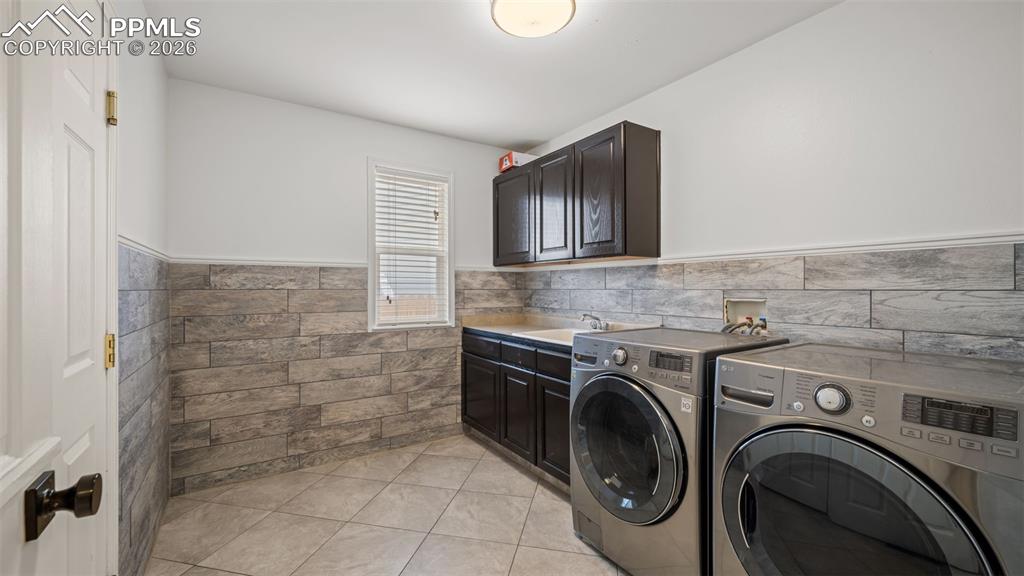 Laundry room featuring wainscoting, washer and dryer, cabinet space, light tile patterned flooring, and tile walls
