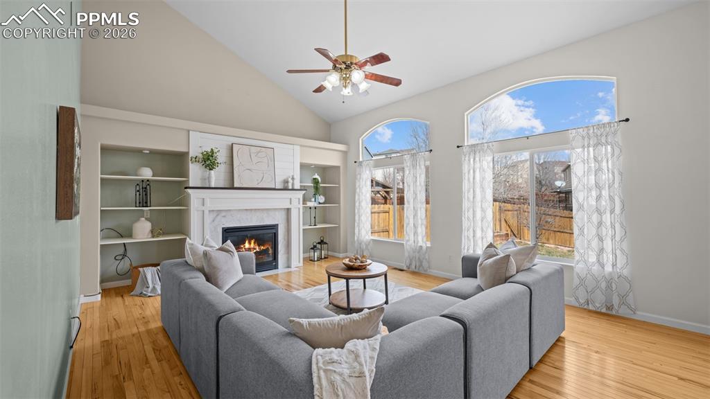 Living area featuring light wood finished floors, a ceiling fan, vaulted ceiling, and a fireplace with flush hearth