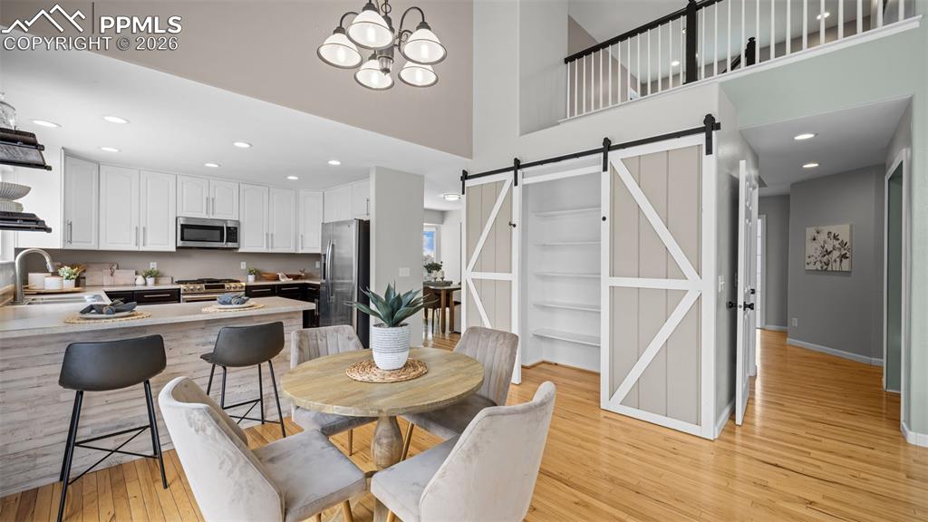 Dining area featuring a barn door, light wood-type flooring, a high ceiling, and a chandelier