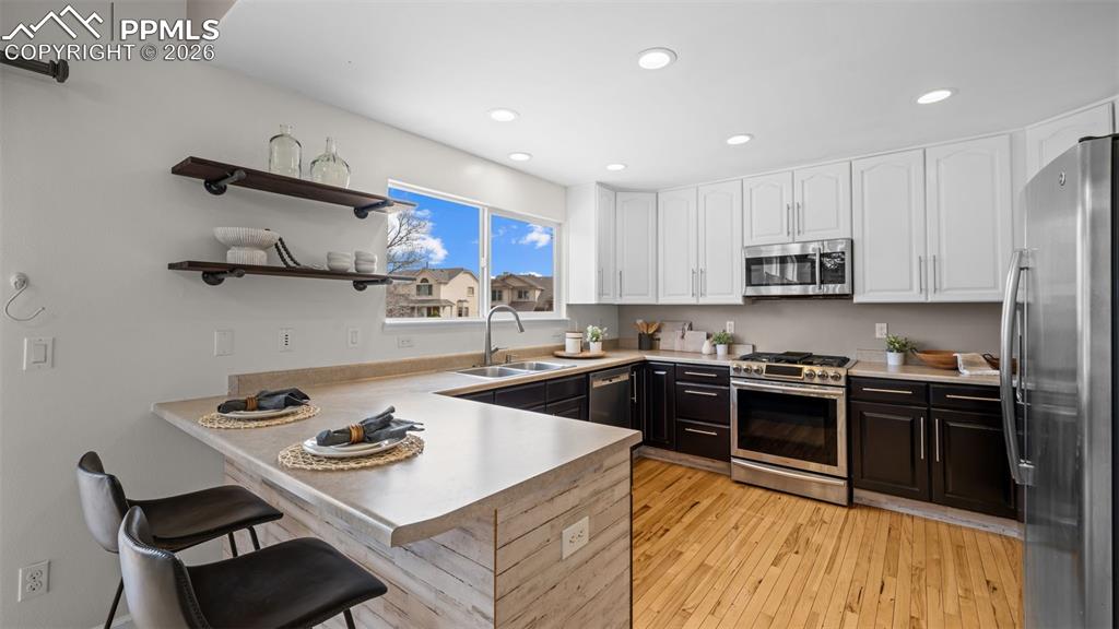Kitchen with a peninsula, stainless steel appliances, two tone cabinets, a breakfast bar, and light wood finished floors