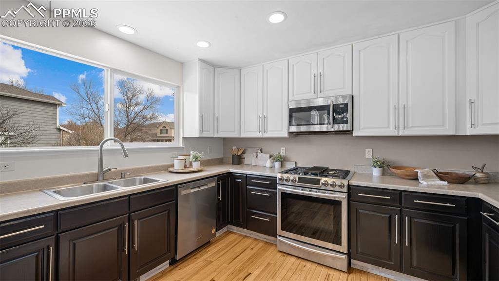 Dual tone kitchen with two tone cabinets, stainless steel appliances, light countertops, light wood-style flooring, and recessed lighting