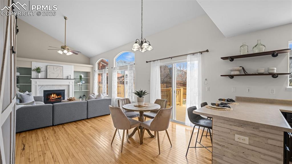 Dining area featuring lofted ceiling, a glass covered fireplace, light wood-type flooring, a ceiling fan, and hanging lights