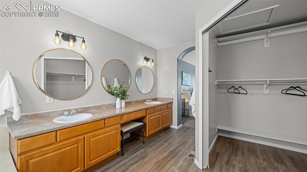 Bathroom featuring a spacious closet, double vanity, connected bathroom, and dark wood-type flooring
