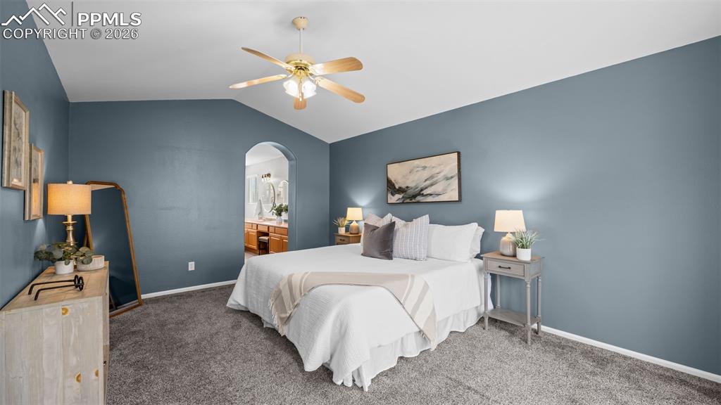Bedroom with arched walkways, vaulted ceiling, a ceiling fan, dark carpet, and connected bathroom