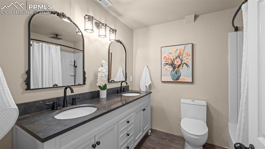 Full bath featuring double vanity, dark wood finished floors, and shower / bathtub combination with curtain