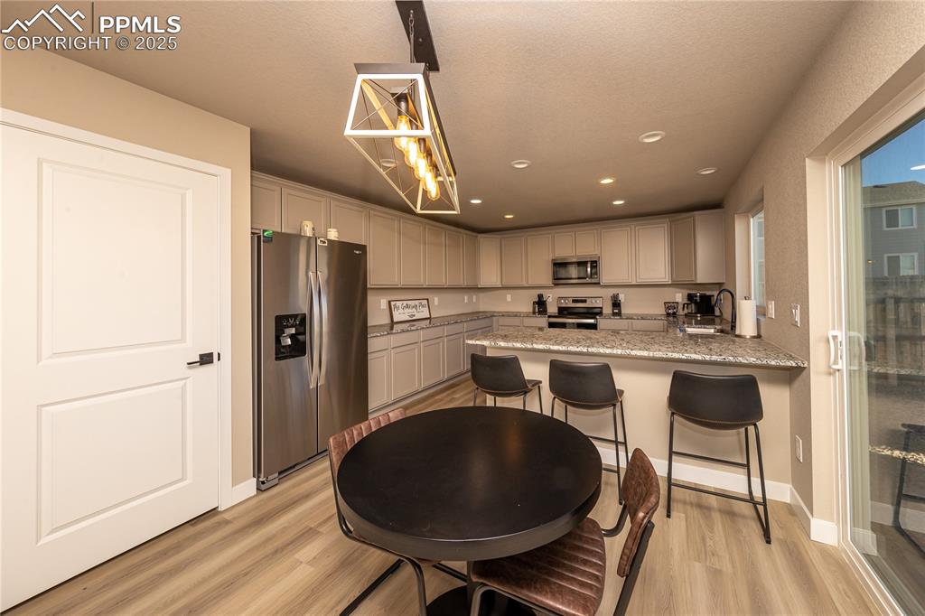 Kitchen with stainless steel appliances, light wood-style floors, a kitchen bar, hanging light fixtures, and recessed lighting
