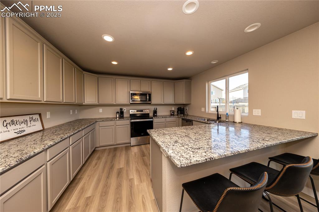 Kitchen with a breakfast bar, light stone countertops, appliances with stainless steel finishes, recessed lighting, and light wood-style floors