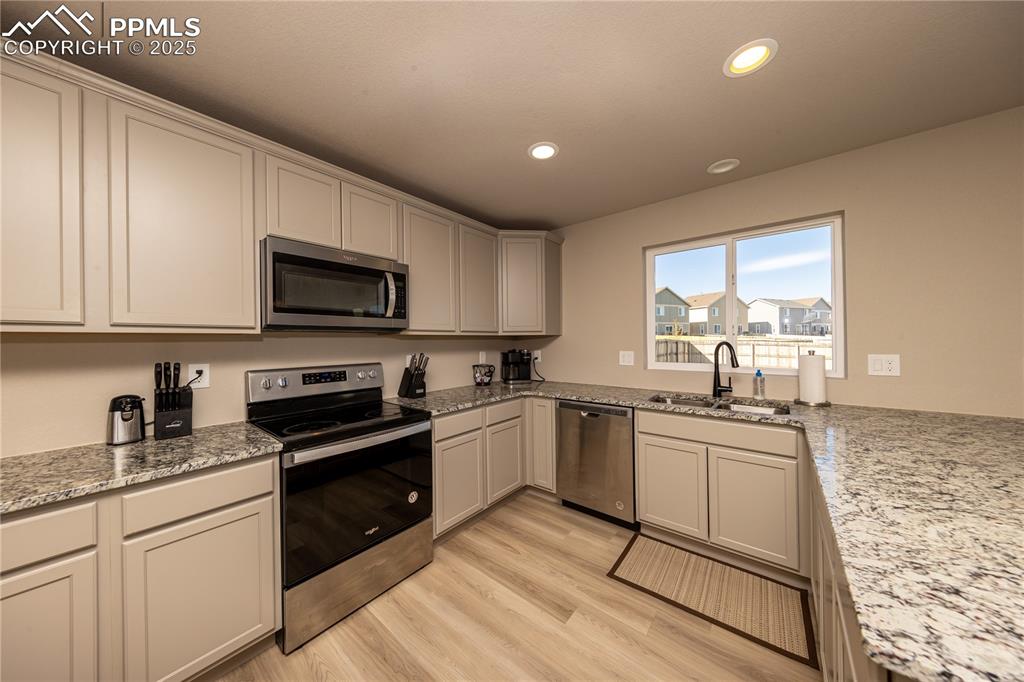 Kitchen featuring appliances with stainless steel finishes, recessed lighting, light stone counters, and light wood finished floors