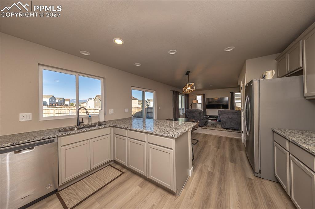 Kitchen with appliances with stainless steel finishes, light stone countertops, a peninsula, decorative light fixtures, and light wood-style flooring