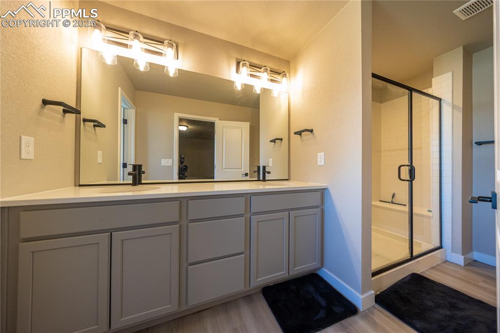 Full bath featuring a textured wall, a stall shower, light wood-type flooring, and double vanity