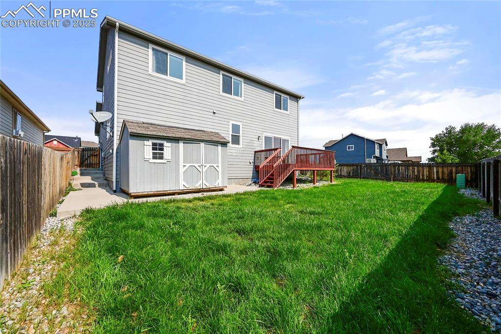 Back of house featuring a fenced backyard, a storage shed, a wooden deck, and stairs