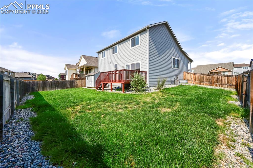 Rear view of house with a deck, a fenced backyard, a storage shed, and a residential view