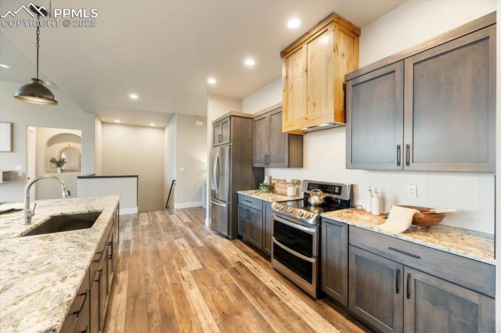 Kitchen with light wood-style flooring, a sink, light stone counters, and appliances with stainless steel finishes