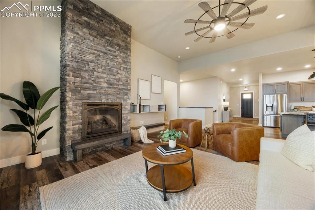 Living room with recessed lighting, wood finished floors, a stone fireplace, baseboards, and a ceiling fan