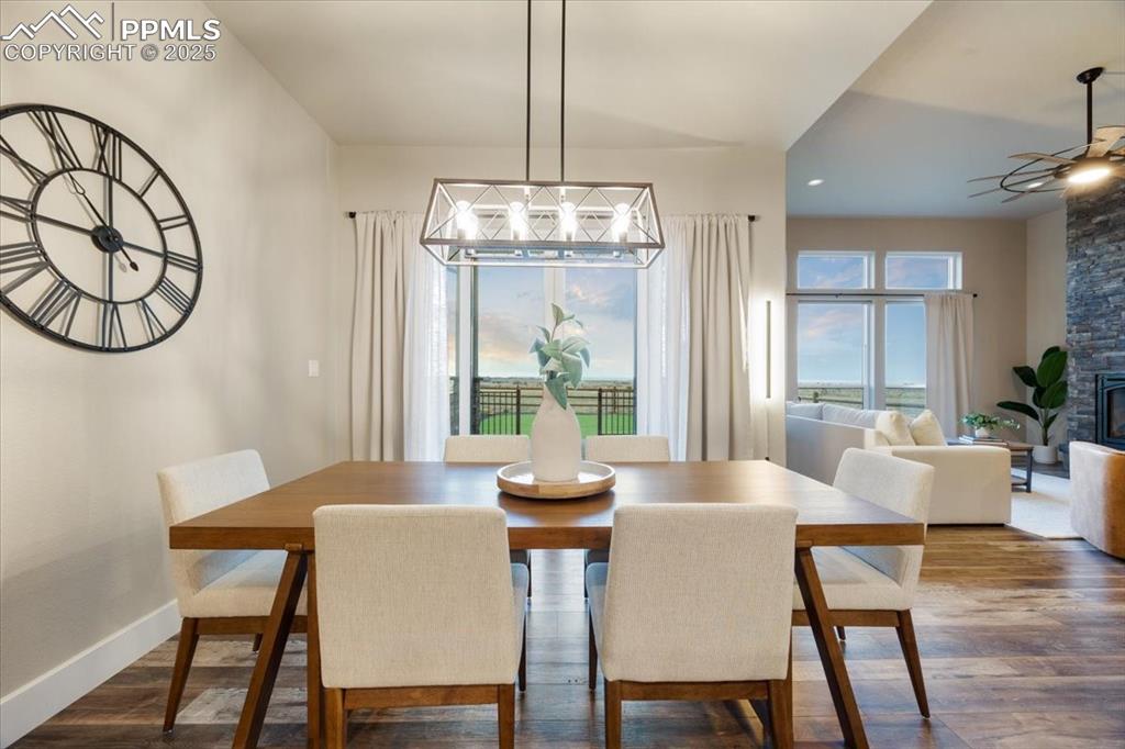 Dining area featuring a fireplace, ceiling fan with notable chandelier, dark wood-style floors, and baseboards
