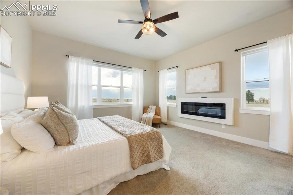 Carpeted bedroom featuring a glass covered fireplace, ceiling fan, and baseboards