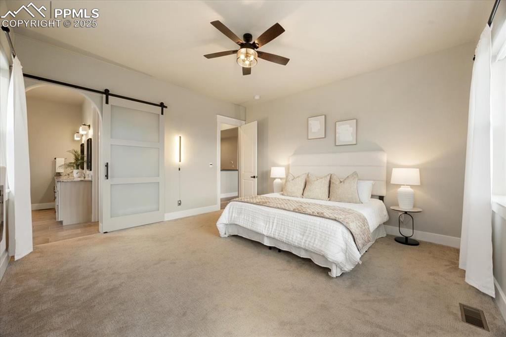 Bedroom with light colored carpet, a barn door, visible vents, arched walkways, and baseboards