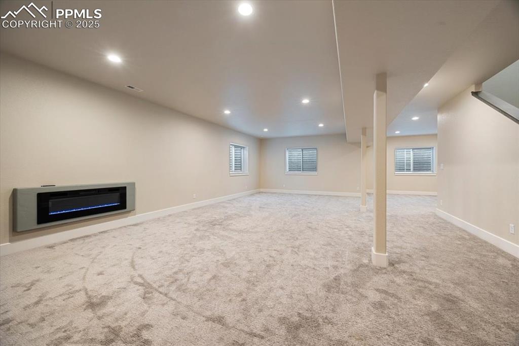 Below grade area with recessed lighting, a glass covered fireplace, visible vents, carpet, and baseboards