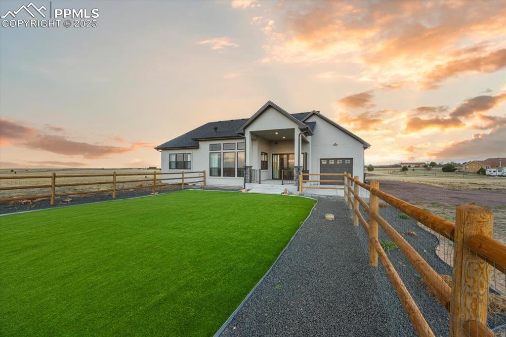 Back of house at dusk featuring driveway, a fenced backyard, stucco siding, a yard, and a garage