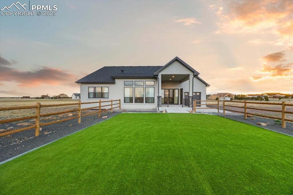 Rear view of house with a lawn, roof with shingles, stucco siding, and a fenced backyard