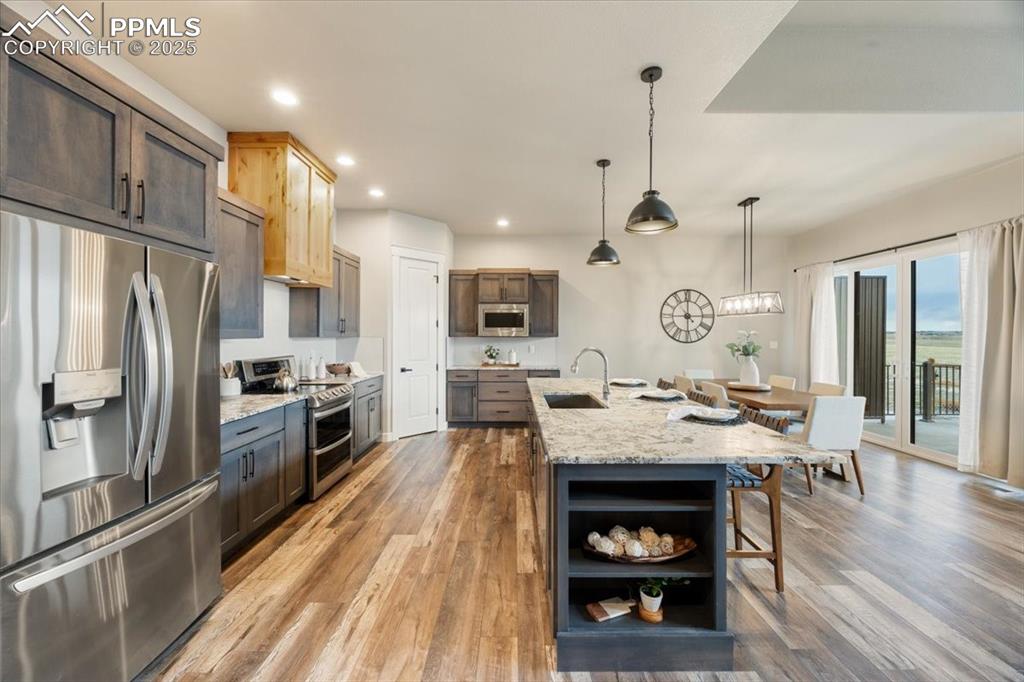 Kitchen featuring light wood-style flooring, a sink, appliances with stainless steel finishes, a breakfast bar, and decorative light fixtures