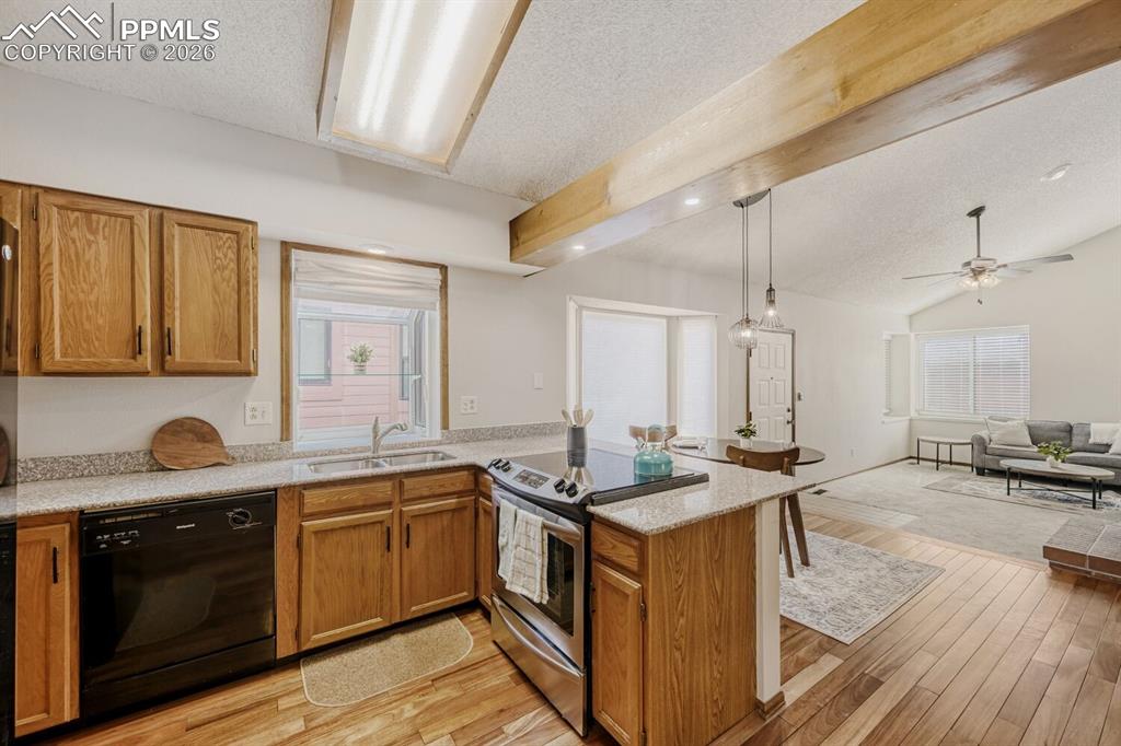 Kitchen featuring stainless steel range with electric cooktop, wood finish cabinetry, a peninsula, dishwasher, and hanging light fixtures