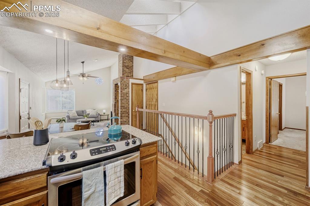 Kitchen with stainless steel electric stove, light wood-style floors, vaulted ceiling with beams, wood finish cabinetry, and a ceiling fan