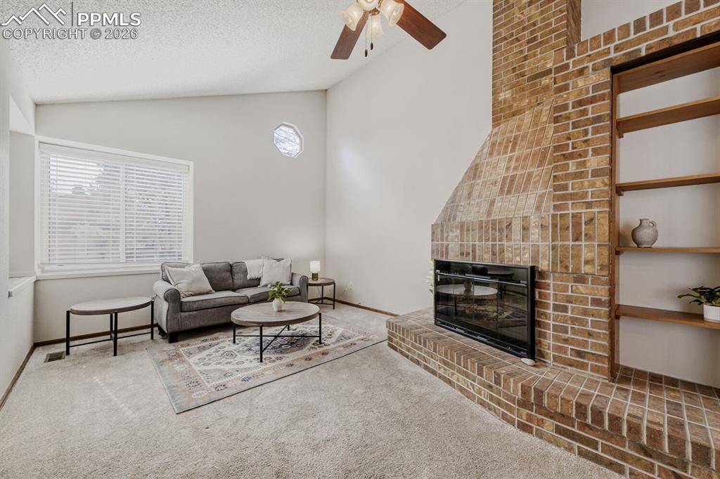 Carpeted living room with a ceiling fan and a glass covered fireplace
