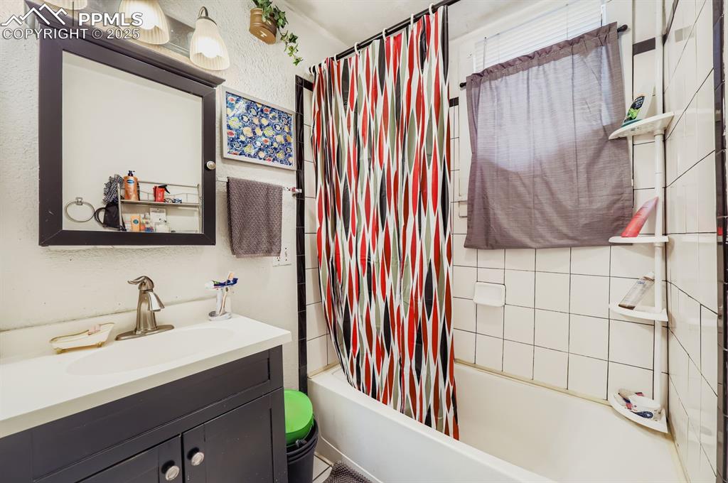 Bathroom featuring shower / tub combo, vanity, and a textured wall