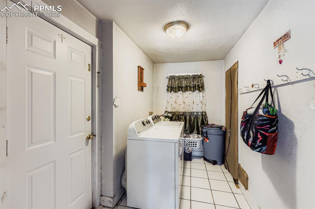Laundry area featuring a textured ceiling, light tile patterned flooring, and washing machine and clothes dryer