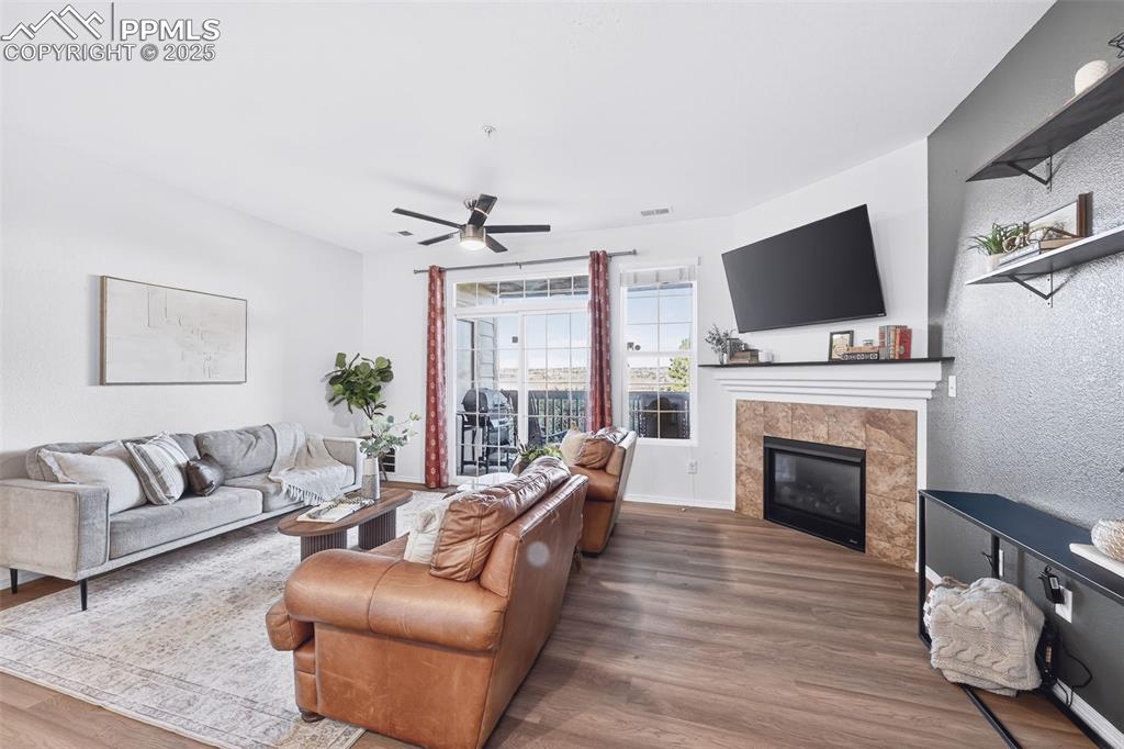 Living area with wood finished floors, a tiled fireplace, ceiling fan, and a textured wall
