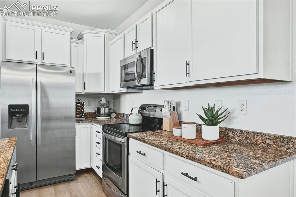 Kitchen featuring stainless steel appliances, white cabinetry, light wood finished floors, and dark stone countertops