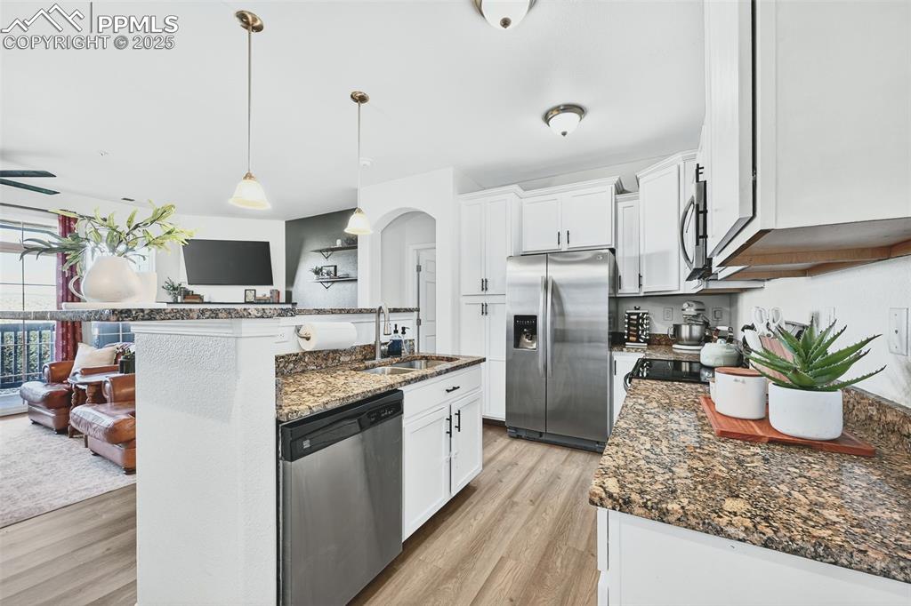 Kitchen with dark stone counters, stainless steel appliances, hanging light fixtures, white cabinets, and light wood-style flooring