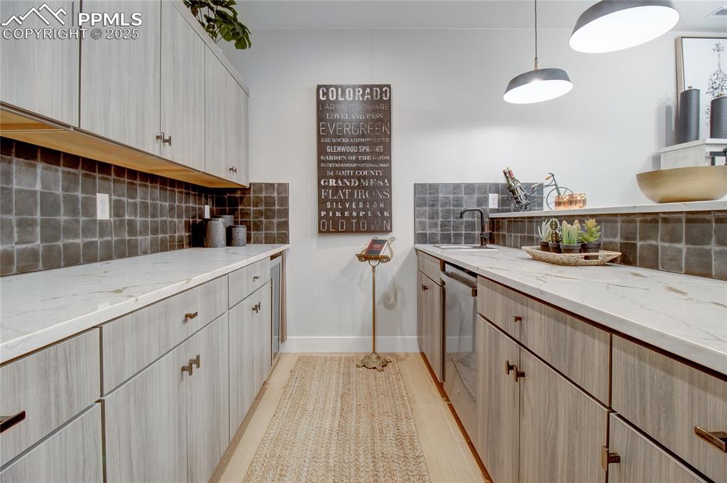 Kitchen with tasteful backsplash, light stone counters, stainless steel dishwasher, and hanging light fixtures