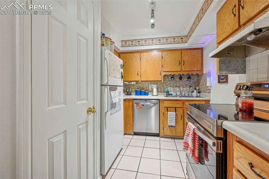 Kitchen with backsplash, stainless steel appliances, brown cabinets, and light tile patterned floors