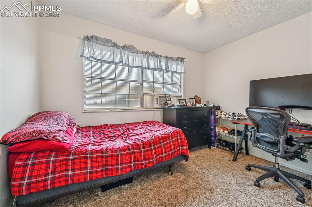 Bedroom featuring carpet, a ceiling fan, a textured ceiling, a desk, and cooling unit