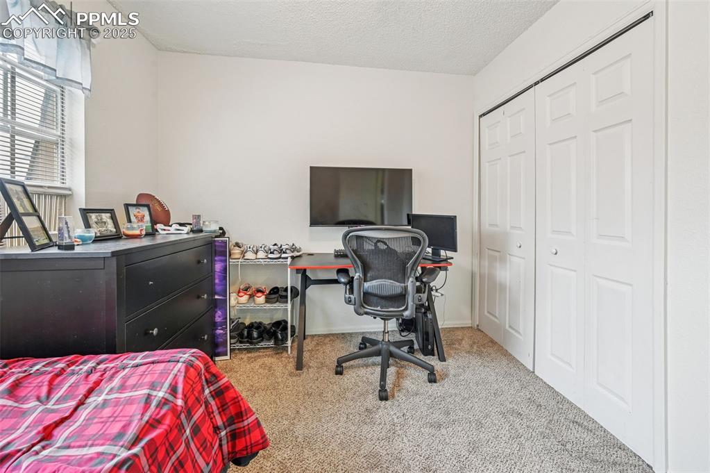 Bedroom featuring light carpet, an office area, a closet, and a textured ceiling