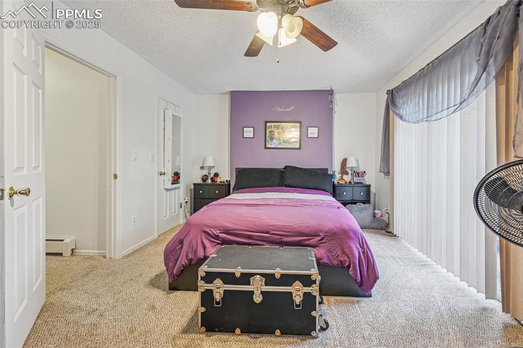 Carpeted bedroom featuring a textured ceiling, a baseboard radiator, and a ceiling fan