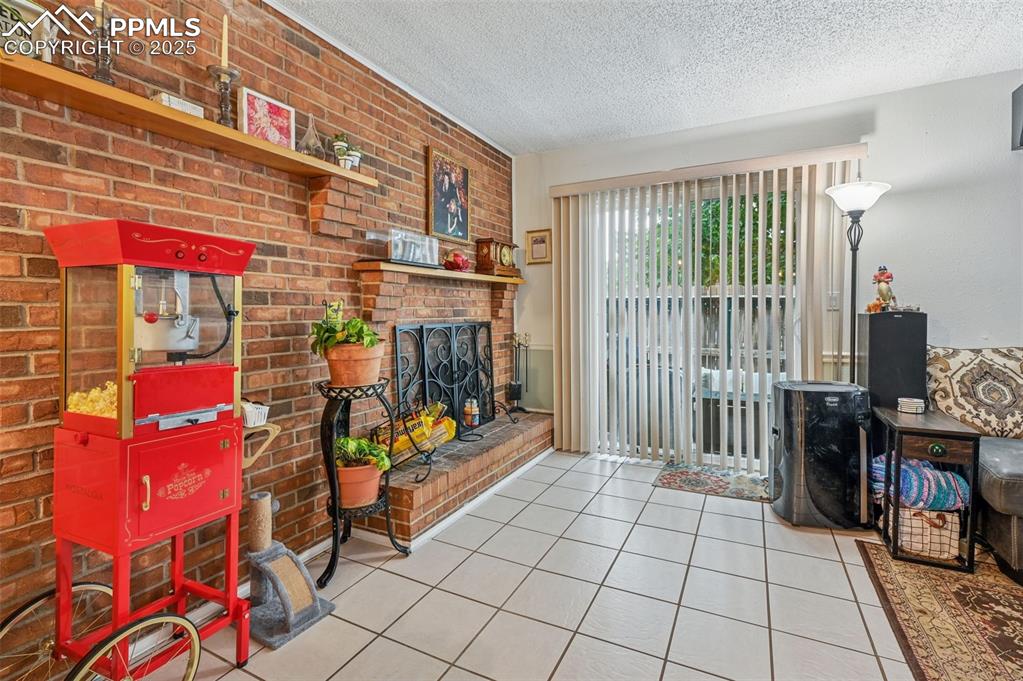 Living room with a textured ceiling, tile patterned floors, brick wall, and a fireplace