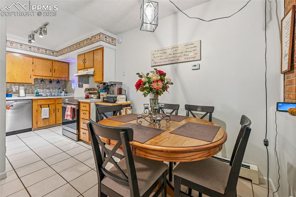 Dining area with light tile patterned floors, a baseboard radiator, a textured ceiling, and track lighting